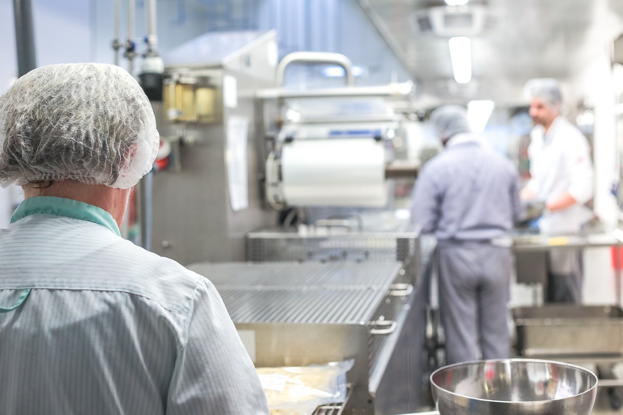 Photograph of a food production line in a factory, with workers wearing hairnets and aprons